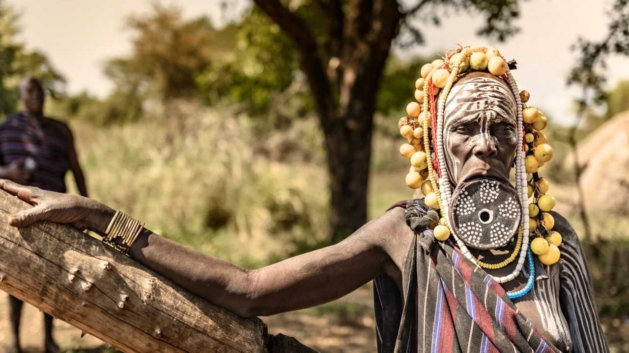 African tribesman leaning on a tree looking into the camera with face painted traditional african tribal colours