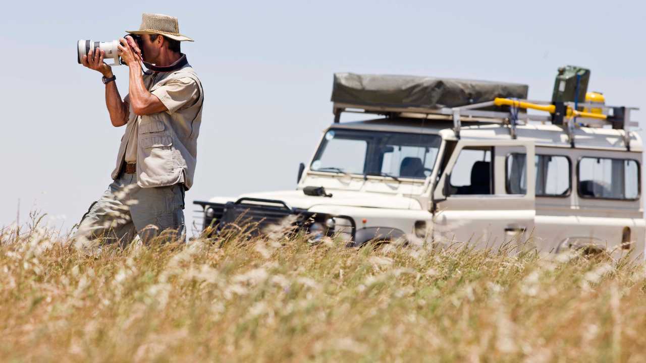 Man with a long lense camera in Africa Savanah with game vehicle in the background taking wildlife photography