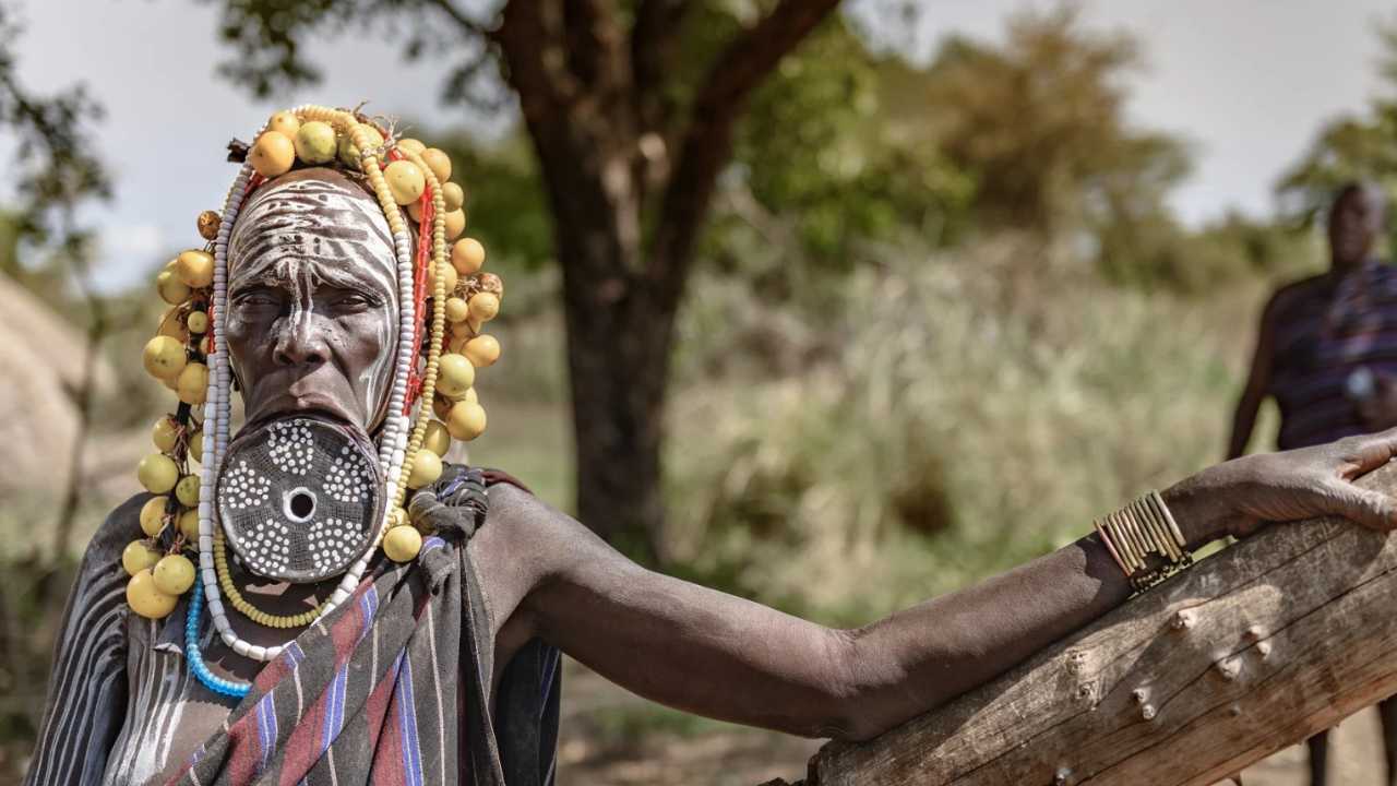 frican tribesman leaning on a tree looking into the camera with face painted traditional african tribal colours
