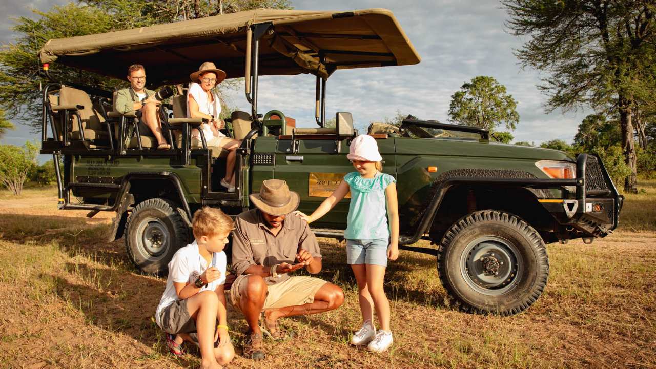 Children with Safari guide looking at a small animal with parents in the background on a game viewing vehicle overlooking the scene
