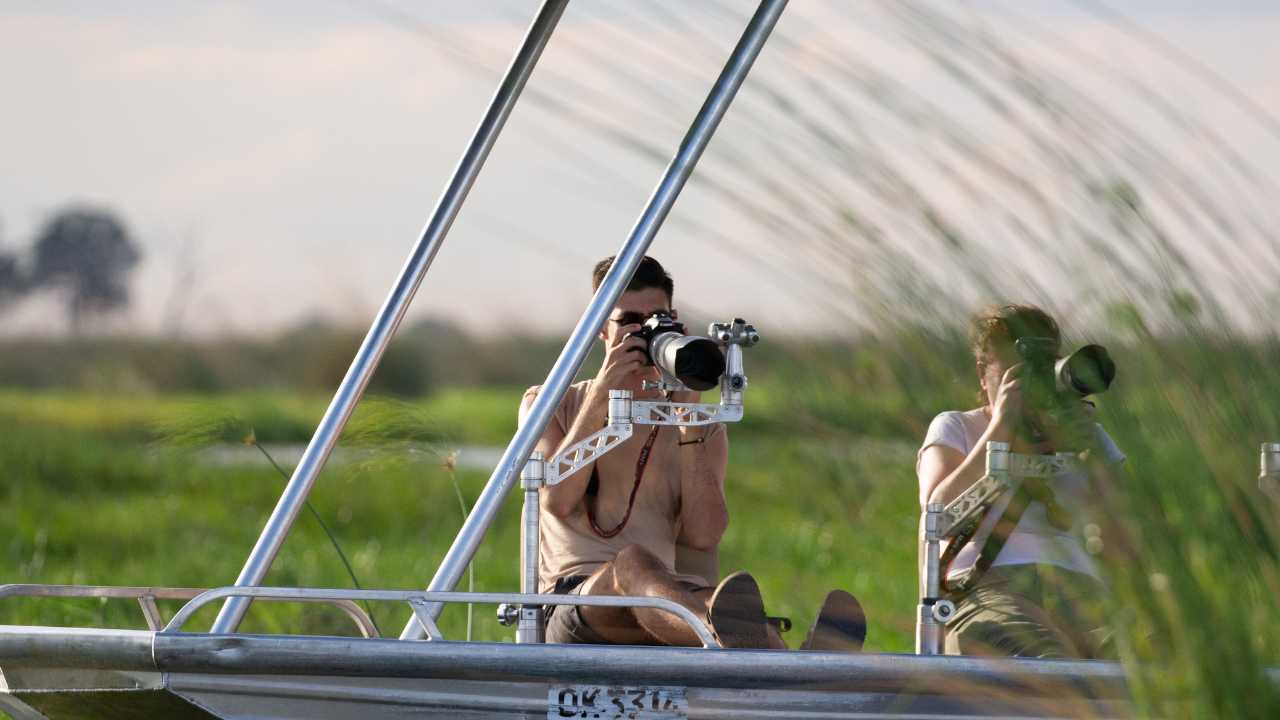 Two wildlife photographers in a floating vessel in the Okavango Delta with long lense camera