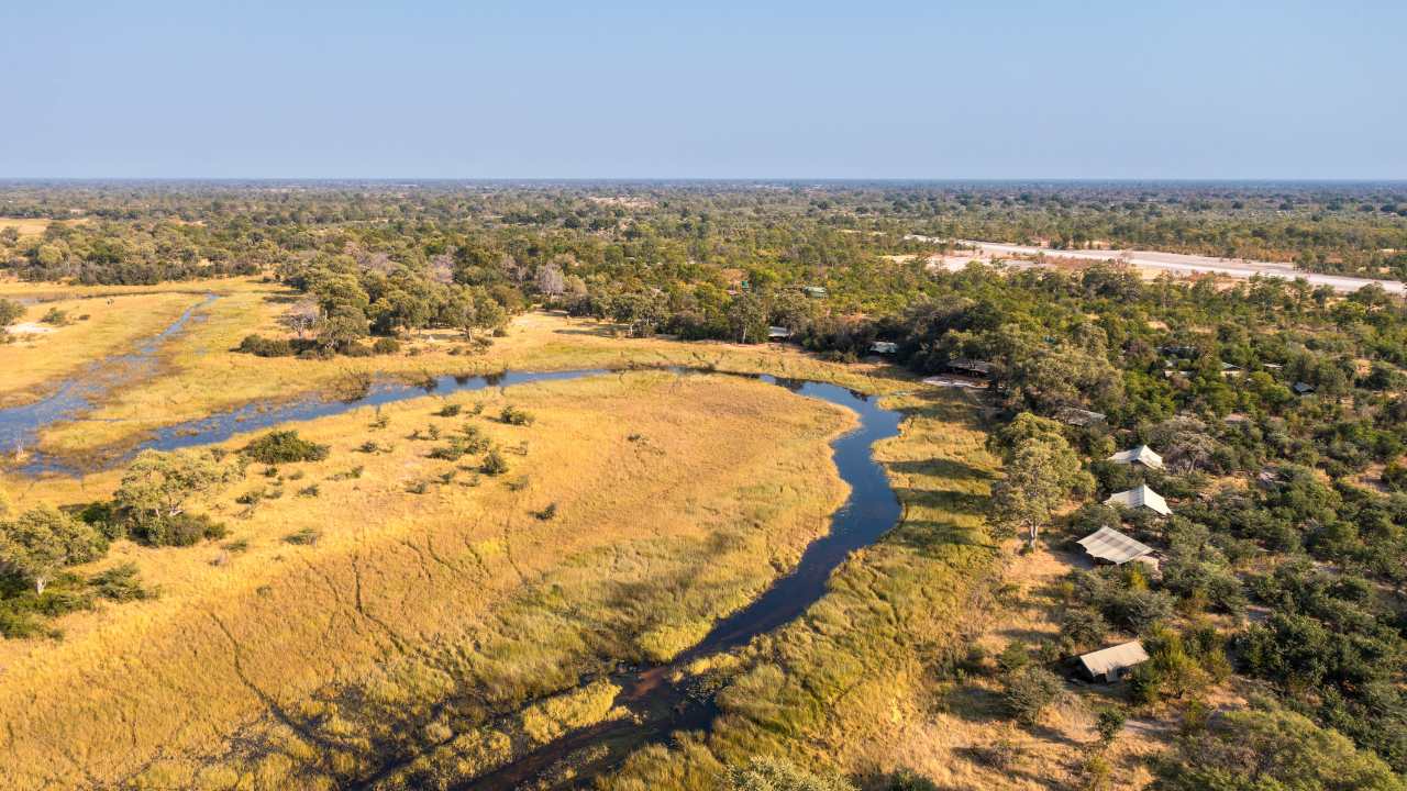 Aerial view of Okavango Explorers Camp in Botswana’s Okavango Delta with bush on the left, camp on the right, and a river running through the middle.