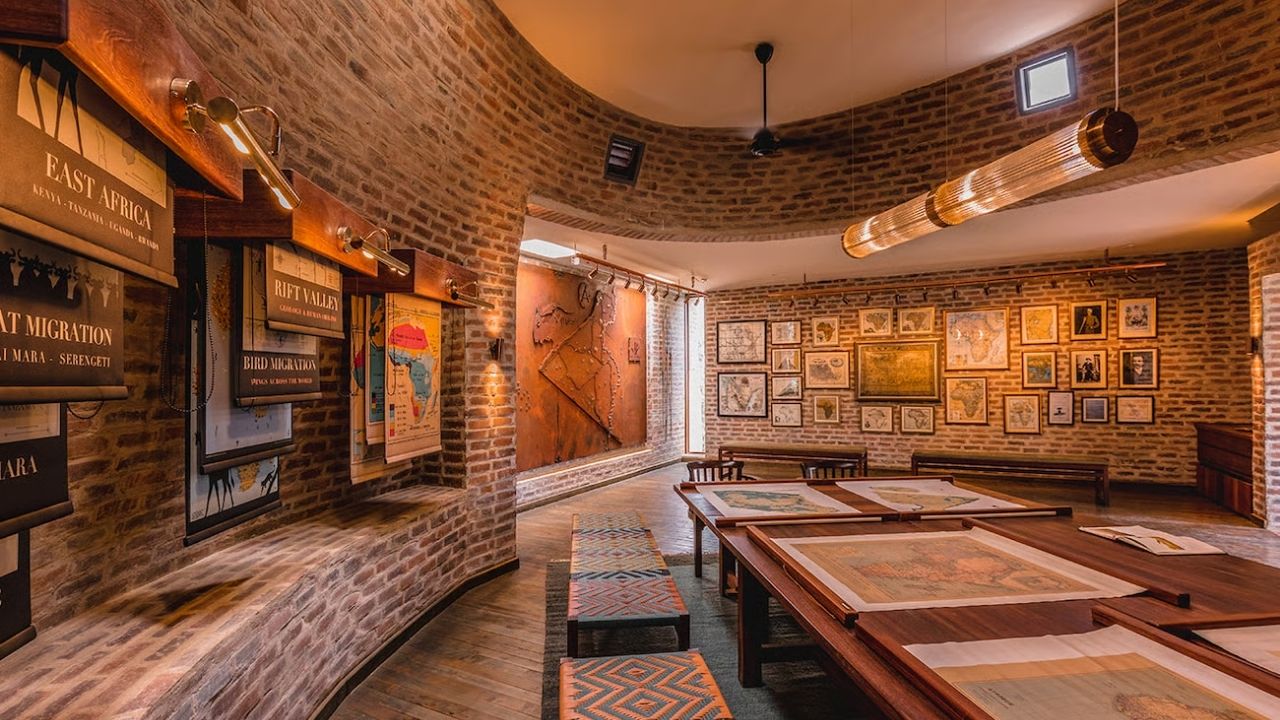 Reception area at Angama Mara Safari Camp, Maasai Mara, Kenya, with wood benches, brick walls, and African maps.