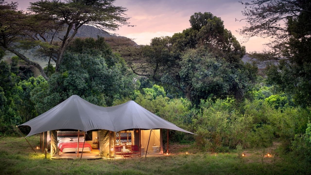 Angama Safari Camp guest suites lit at dusk with African bush in the background, Maasai Mara, Kenya.