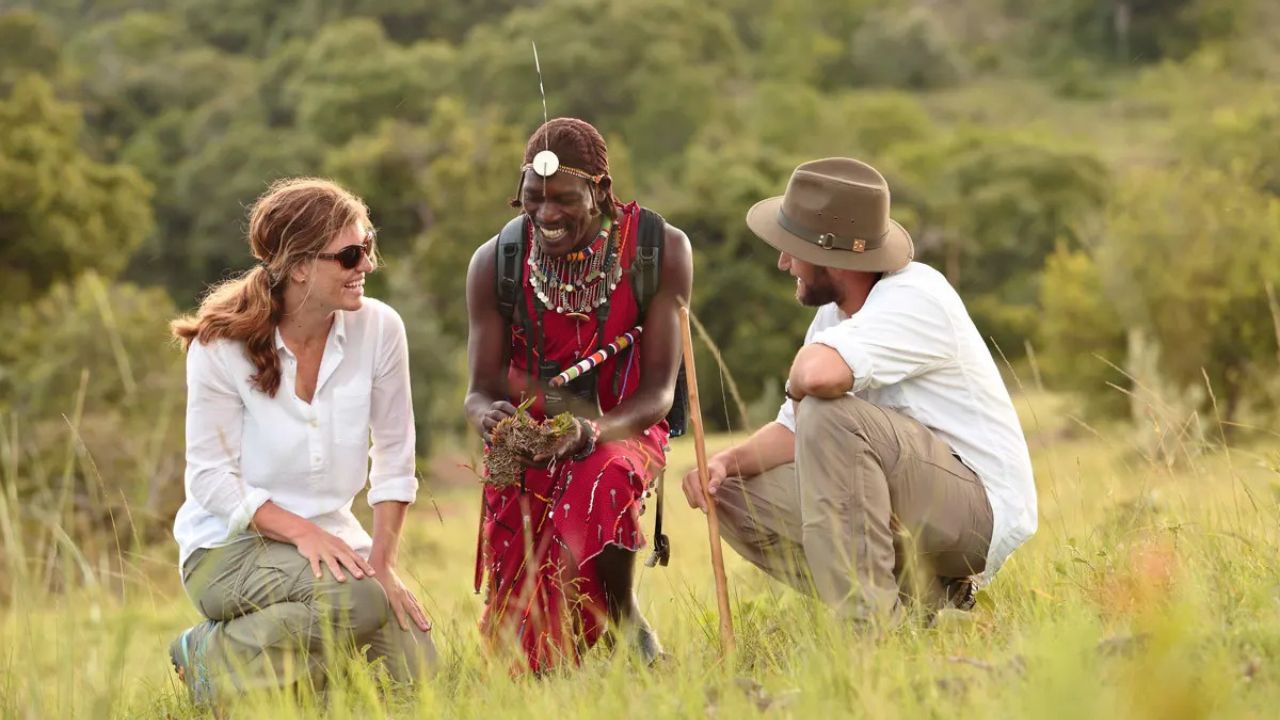 Couple kneeling with Maasai warrior during a bush culture walking safari in Kenya.