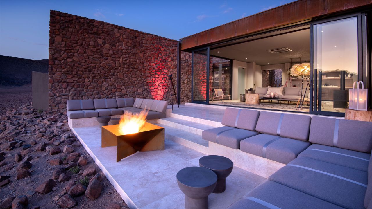 Guest suite terrace with fire and open bay windows overlooking desert at Sossusvlei Desert Lodge