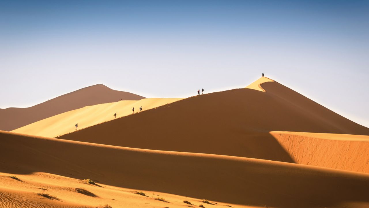 Guests climbing golden sand dunes in the Namib Desert near Sossusvlei Desert Lodge