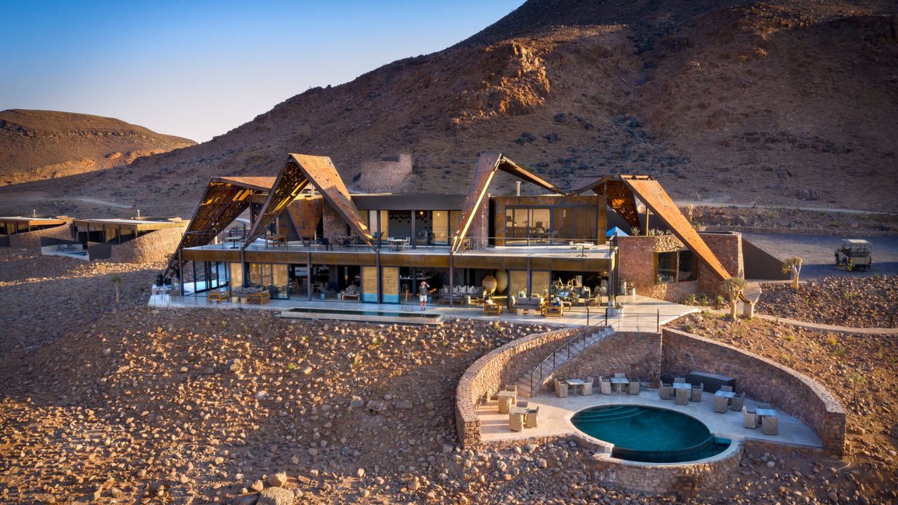 Front view of Sossusvlei Desert Lodge with swimming pool in foreground and desert plains behind