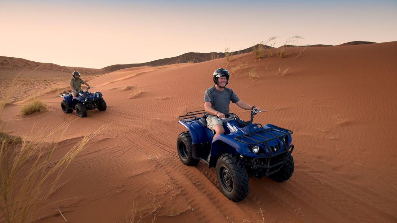 Guests riding quad bikes across red desert dunes at Sossusvlei Desert Lodge