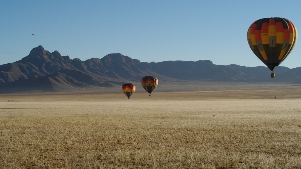 Two hot air balloons floating over Namib Desert, mountains in background