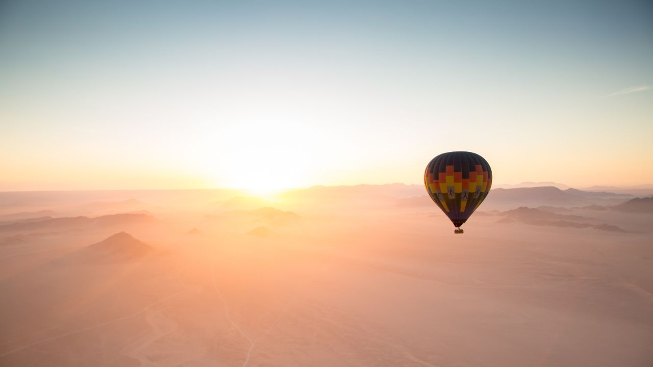 Hot air balloon rising over Namib Desert with sun on horizon