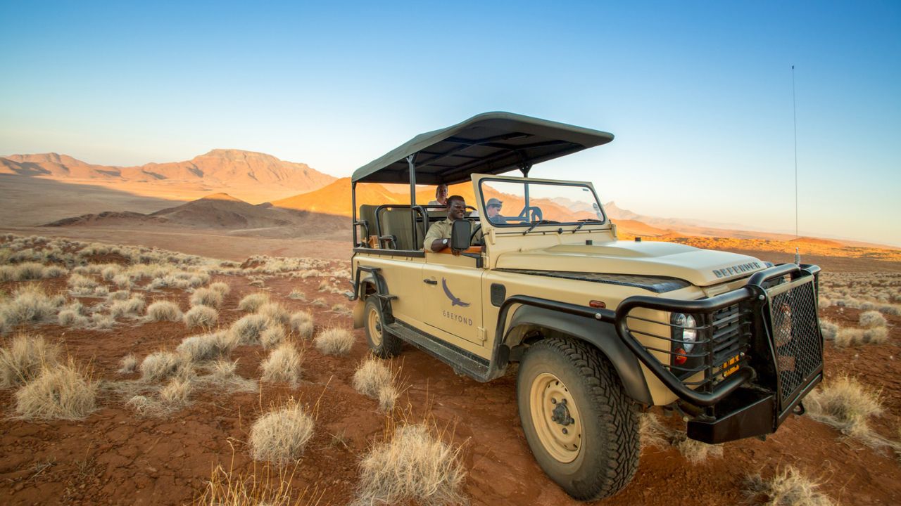 Safari vehicle on game drive through red sand dunes of Namib Desert