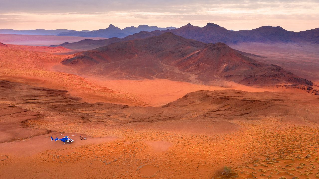 Helicopter flying over Namib Desert dunes and barren red sand landscape