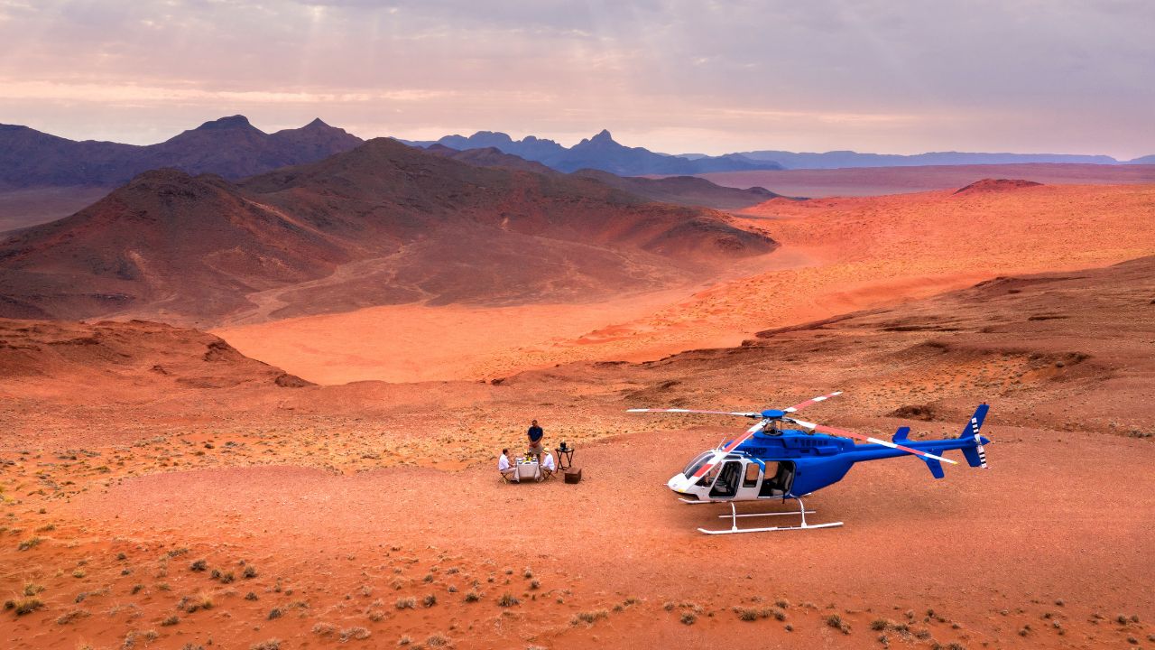Helicopter on red desert sands with guides preparing sundowner drinks, Namibia