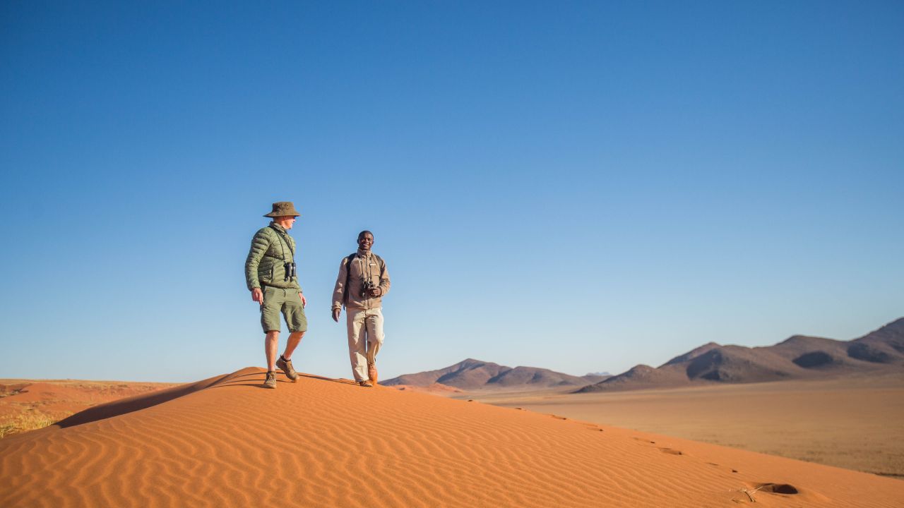 Front view of guests and guide on walking safari across red dunes in Namibia