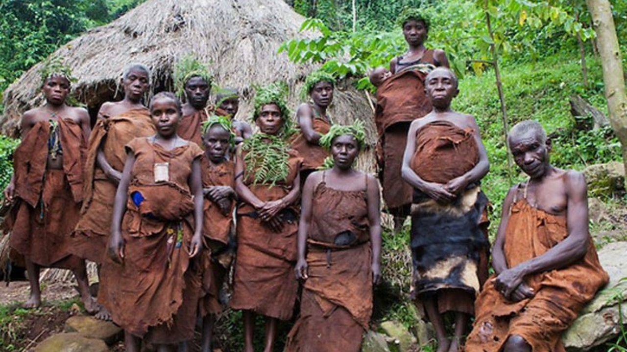 Group of Batwa villagers posing with traditional grass hut