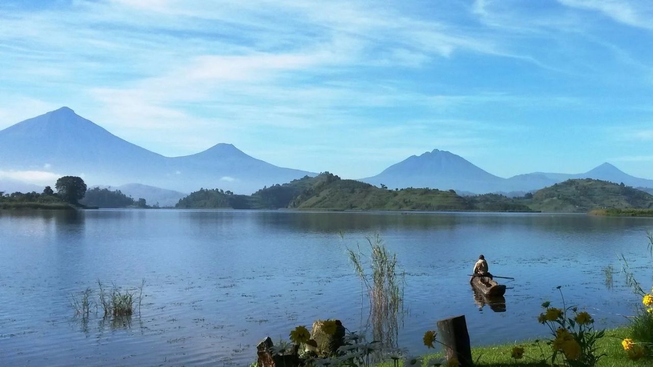 Guide paddling wooden dugout canoe on Lake Mutanda with mountains behind