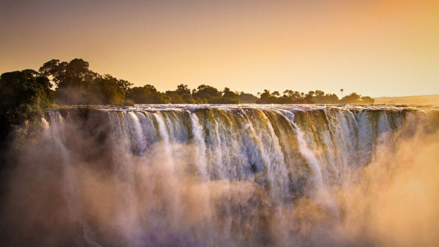Sunset over Victoria Falls with glowing orange skies and full waterfall flow.