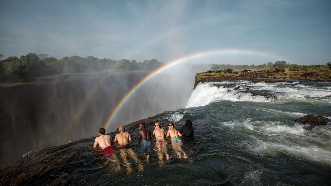 Two guides and four guests at Devil's Pool, Victoria Falls, overlooking falls