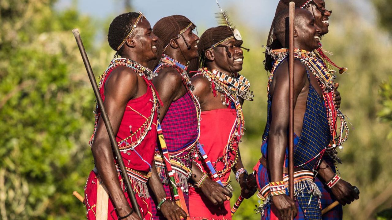 Three Maasai tribesmen standing on elevated rock overlooking the Great Maasai Mara plains, Kenya. Iconic African safari and cultural scene.