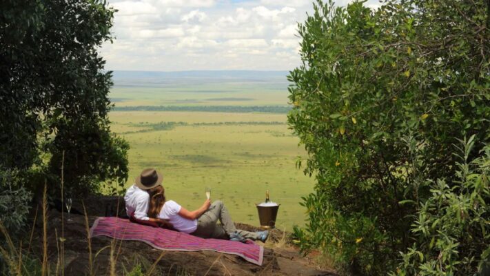 Romantic couple sitting on a rock overlooking the Maasai Plains during a Kenyan safari.