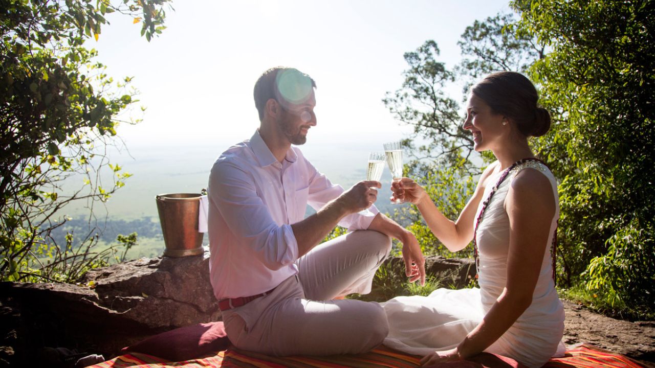 Romantic couple sharing champagne at a viewpoint overlooking the Maasai Mara.