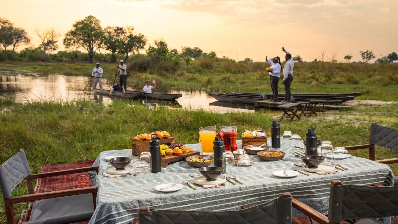 Guests arrive by canoe at Duba Plains Camp and are welcomed by safari hosts to a table with juices and fruits for sundowners, Botswana.