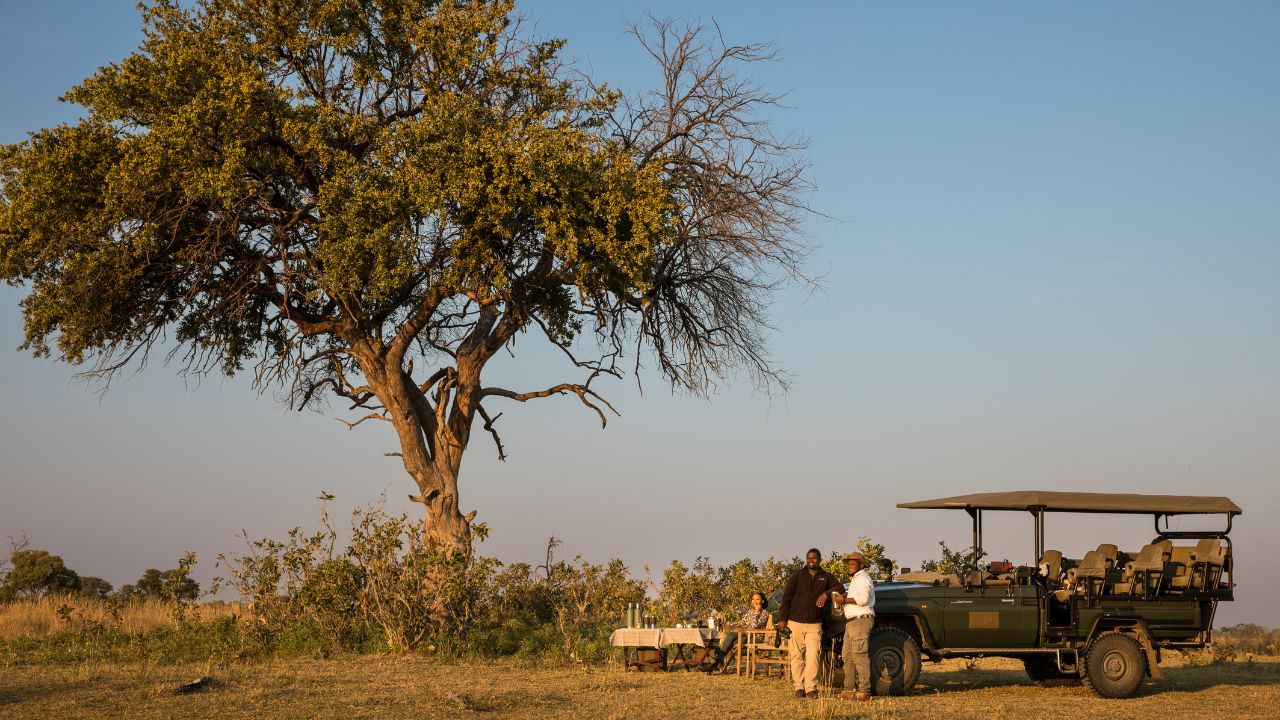 Guests standing with ranger next to safari vehicle enjoying sunset at Zarafa Camp