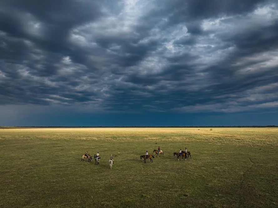 Wide open African plains with aerial shots of people on a horse safari with deep blue sky on open savannah.
