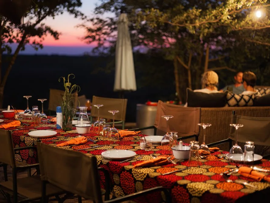 Table set in the sunset of the African bush with red tablecloth, cutlery, as the sun goes down on the African bush.