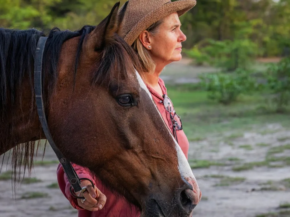 Woman next to horse, observing game next to river on horseback safari.