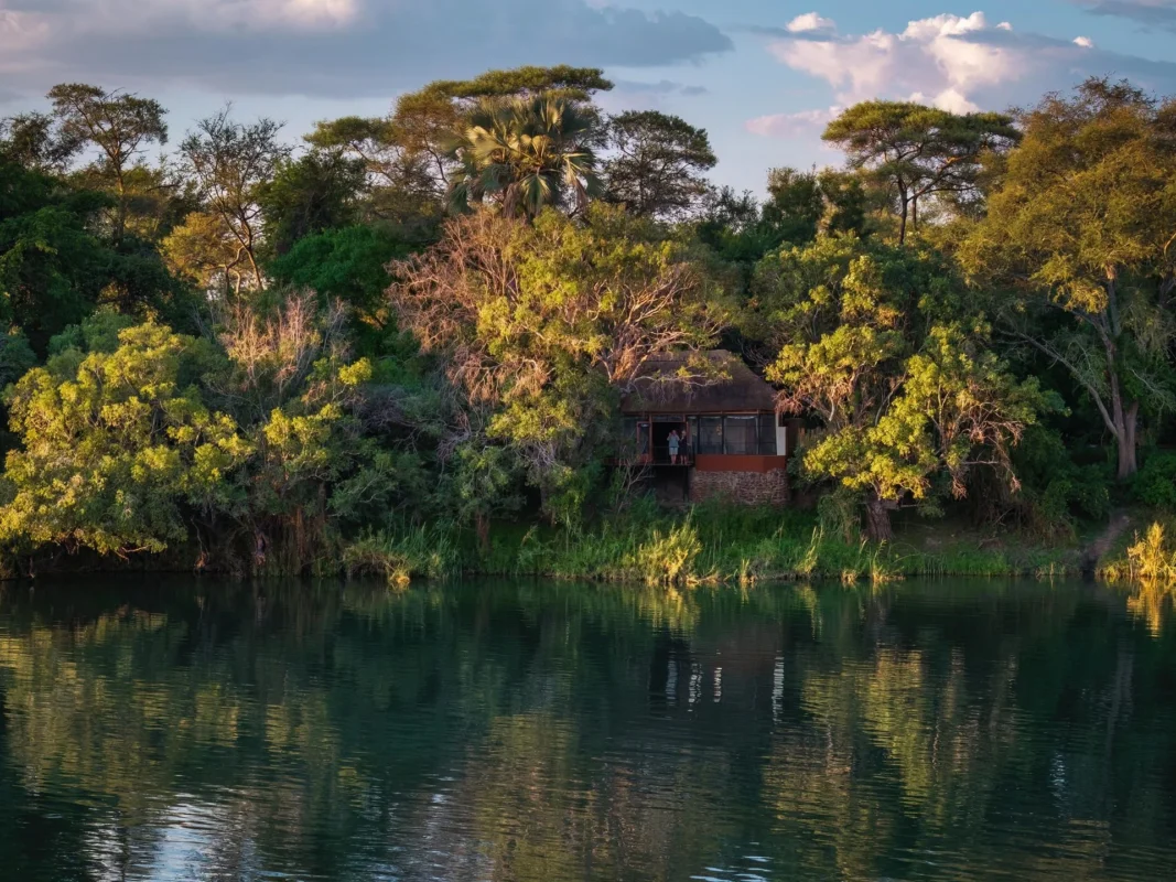 Chundukwa River Lodge in Livingston, viewed from across the river, blue skies and summer thick bush.