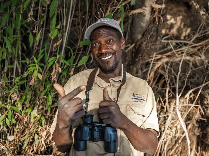 Safari guide with a big smile, holding binoculars around his neck, ready to take guests out on a wildlife safari.