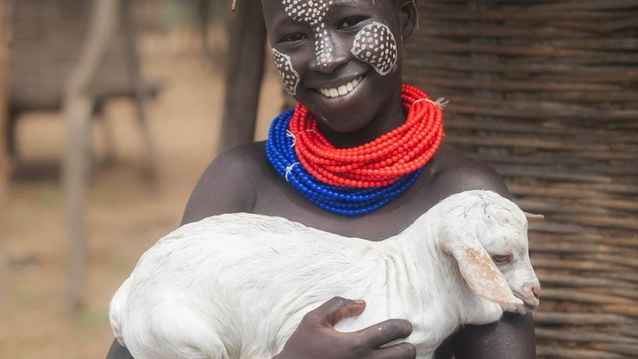 Omo Valley boy holding goat with tribal necklaces and face paint