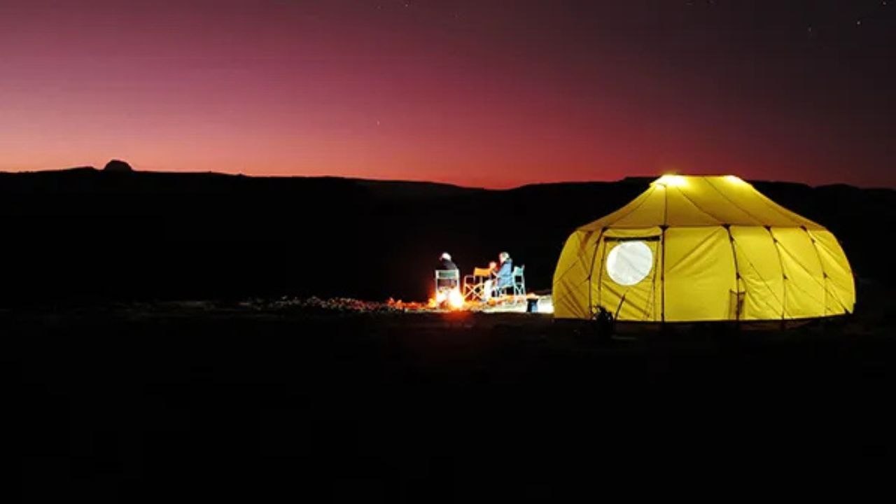 Ethiopian tented camp at sunset, glowing under a red sky with lanterns lighting the tents.