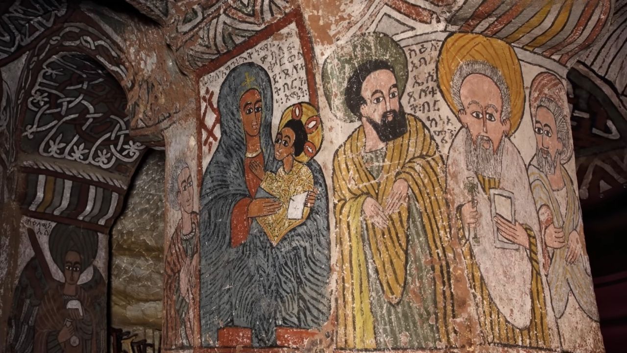 Colorful fresco paintings on interior walls of Abuna Yemata Guh monastery, depicting people and saints.
