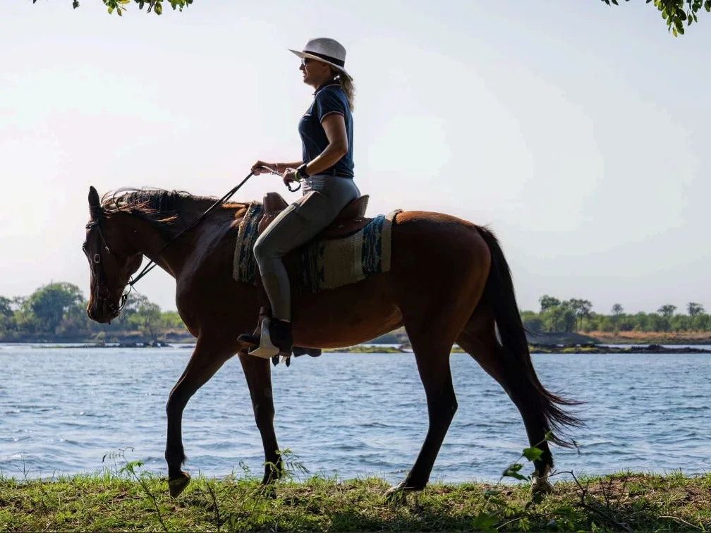 Woman riding a horse along the Zambezi River, with river in the background, Zambia.