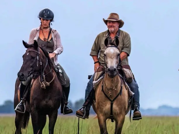 man and woman on horseback riding towards the camera with blue sky in background on African plains in Zambia