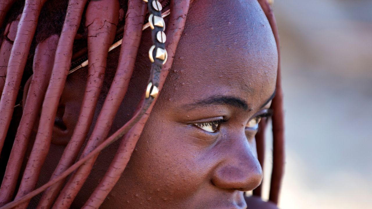 Close-up detail of braided Himba hairstyles coated in otjize with intricate plaits and traditional adornments