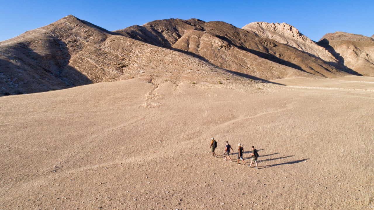 Aerial view of safari guide leading three guests on a walking safari through the desert landscape of northwestern Namibia