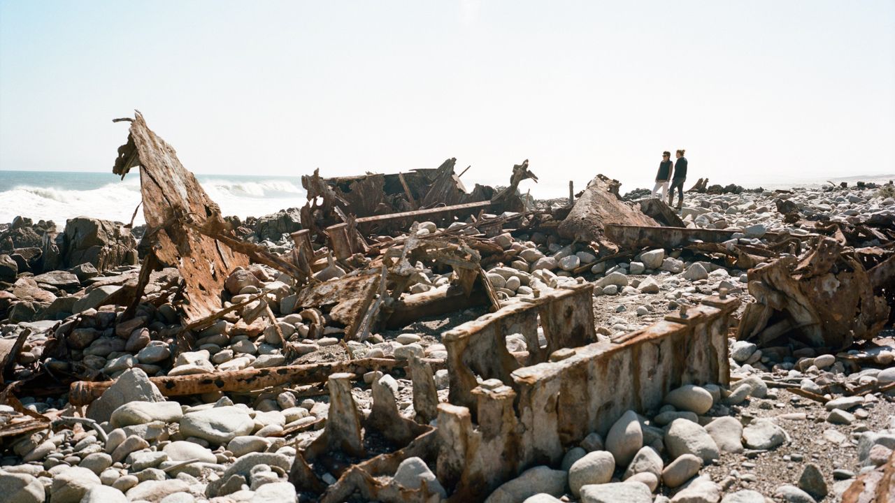 Two guests walking along shipwreck remains on stony beach near Shipwreck Lodge