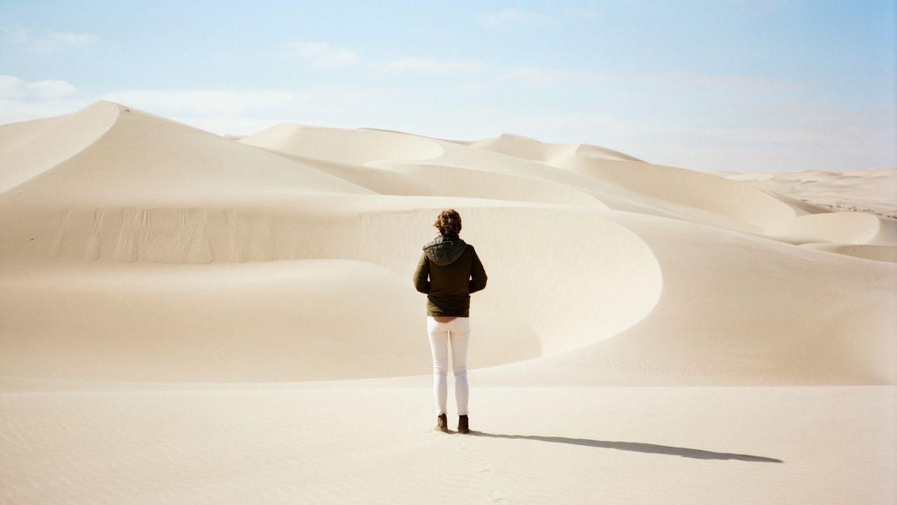 Guests in white pants and blue tops standing on white dunes facing desert