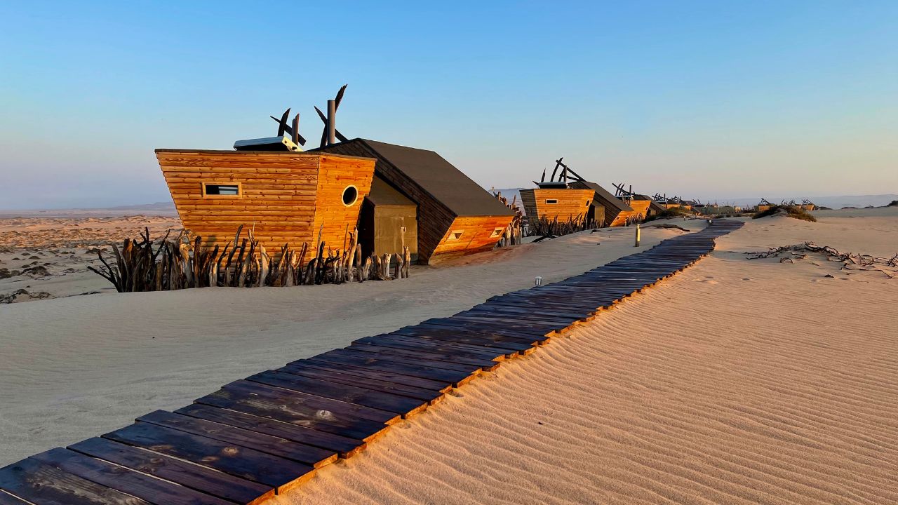 Wooden walkway at Shipwreck Lodge with lodge on left, sand dunes on right