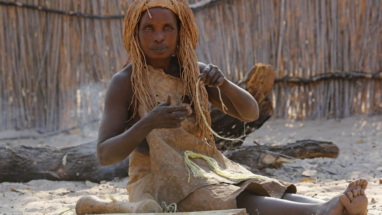 Himba tribal lady sitting weaving basket in desert village