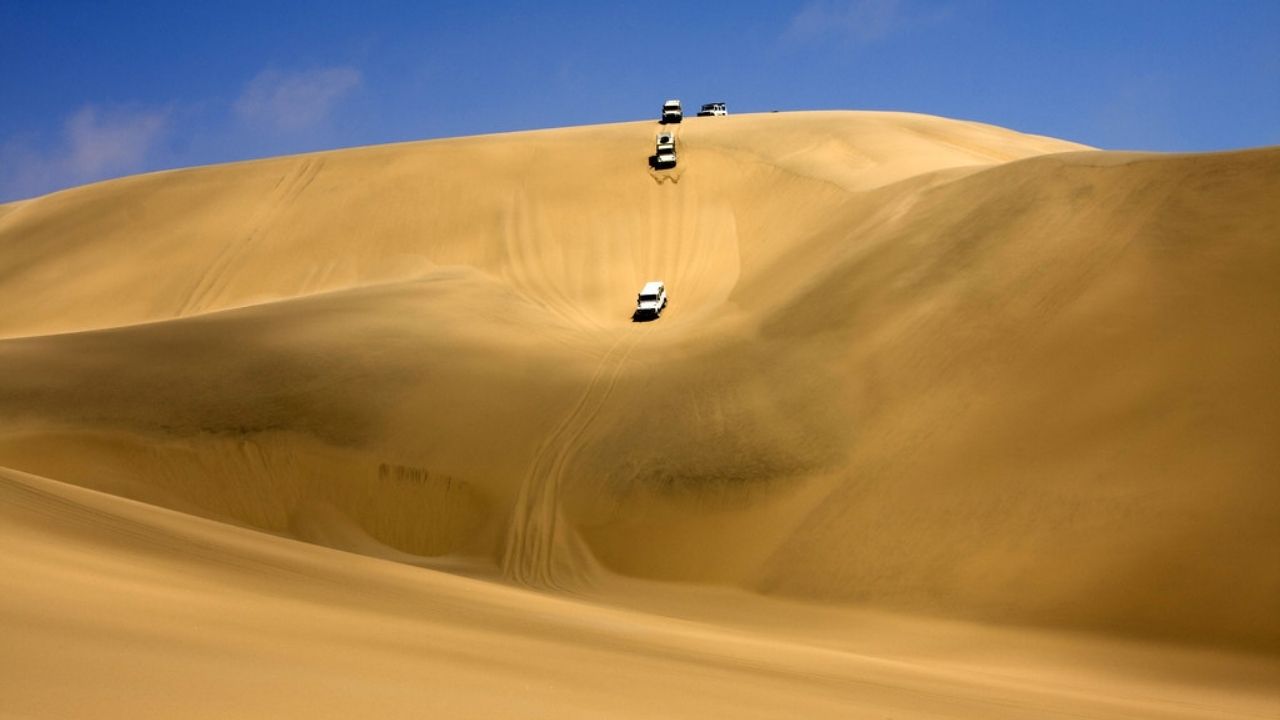 4x4 vehicles driving across golden dunes, deep blue sky, Namibia