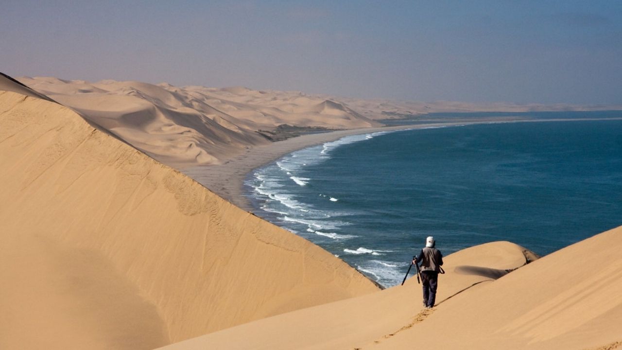 Photographer capturing Skeleton Coast, dunes on left, ocean on right, Namibia