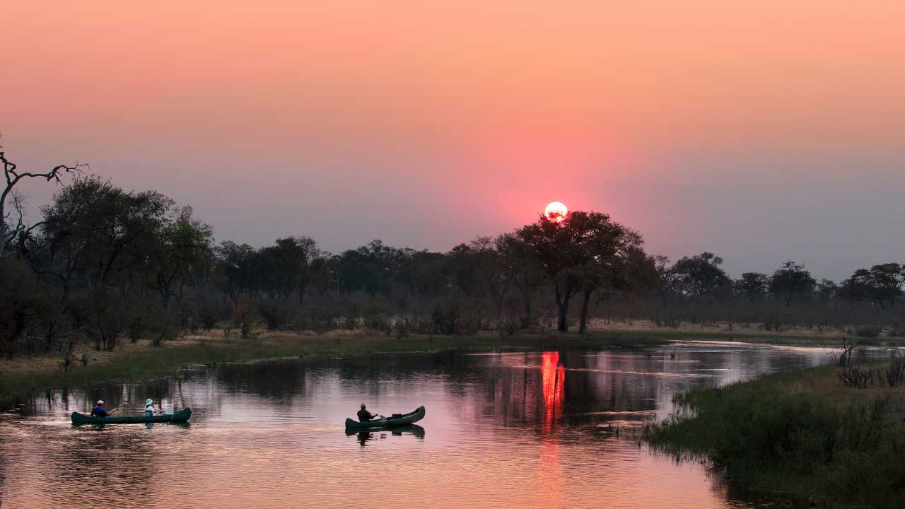 Guests in dugout canoes at Selinda Explorer Camp Botswana at sunset.