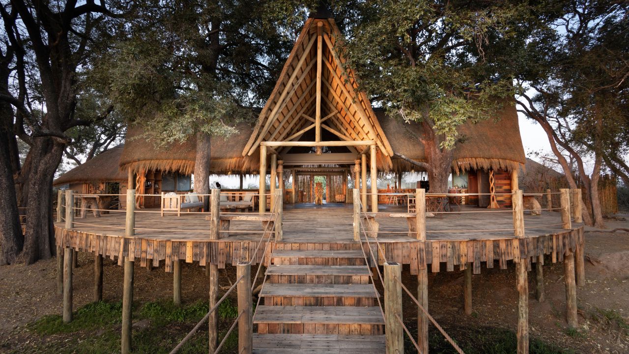 Entrance of Sitatunga Private Island main lodge in Botswana, featuring a thatched roof and wooden doorway, surrounded by tropical vegetation, welcoming guests to a luxury safari experience.