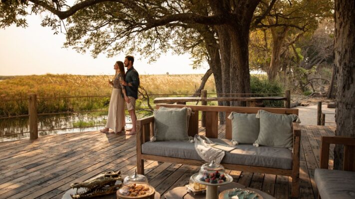Romantic couple enjoying sunset drinks on the deck at Sitatunga Private Island, looking over the Okavango Delta, Botswana.
