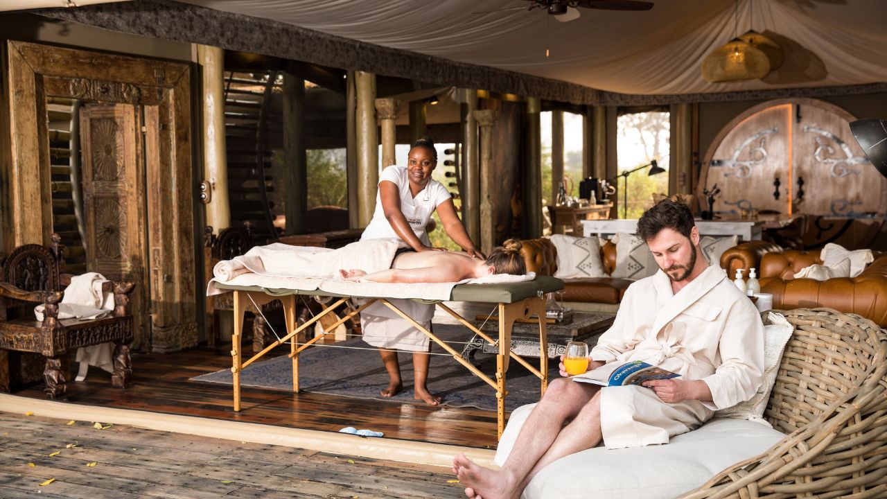 Romantic couple at Sitatunga Private Island, lady on massage table and gentleman reading on deck, Botswana.